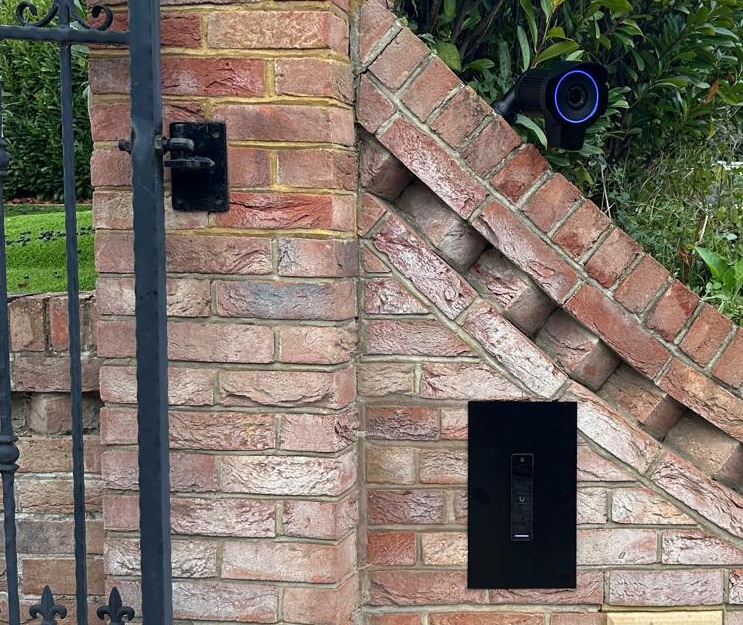Close crop of a UniFi camera and video intercom mounted on a brick gate pillar
